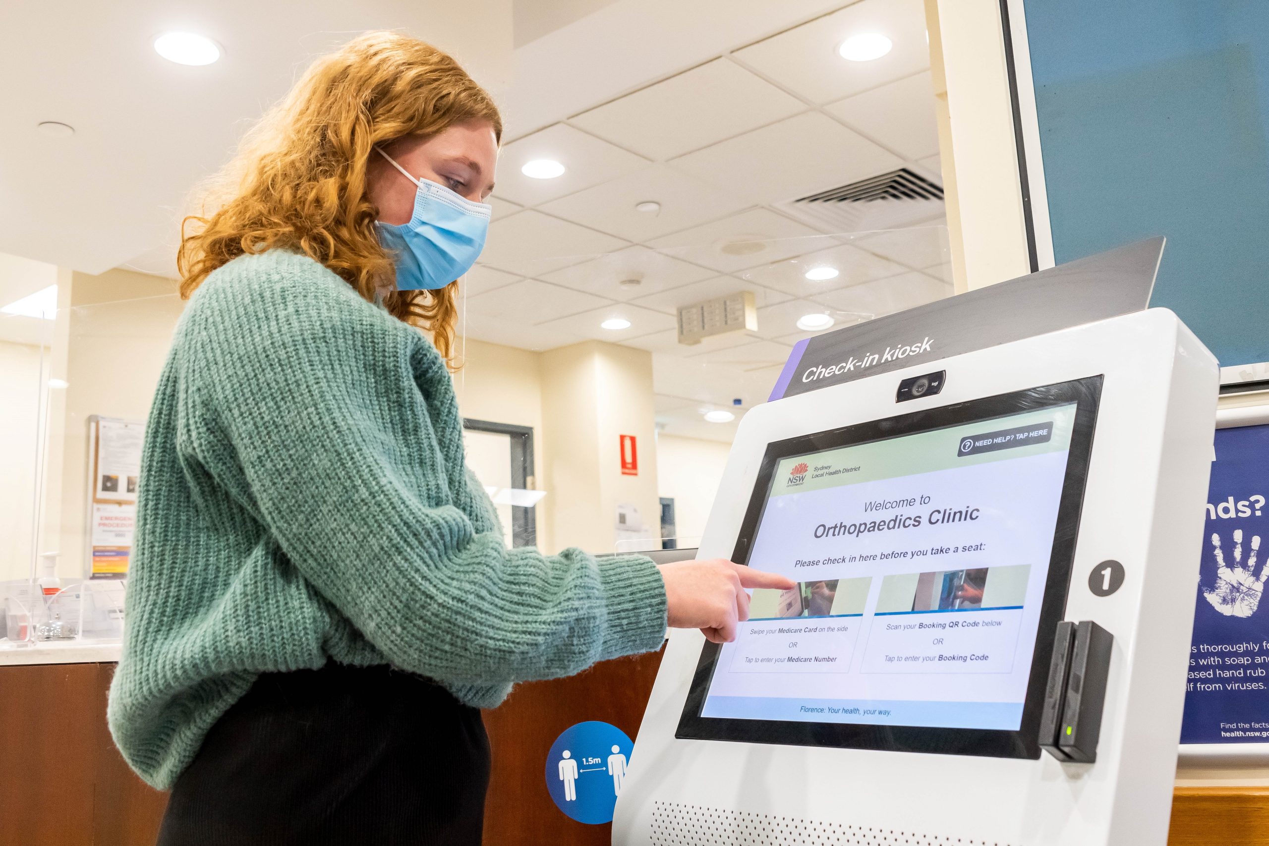 Young lady interacting with digital kiosk screen in hospital clinic