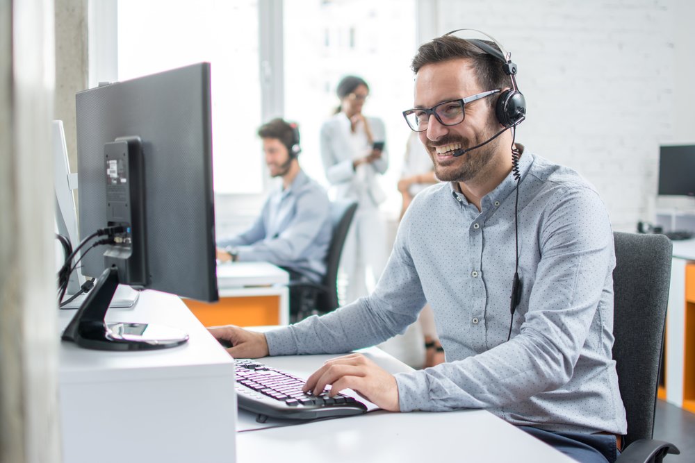 Happy male employee on computer with headset at corporate service organisation