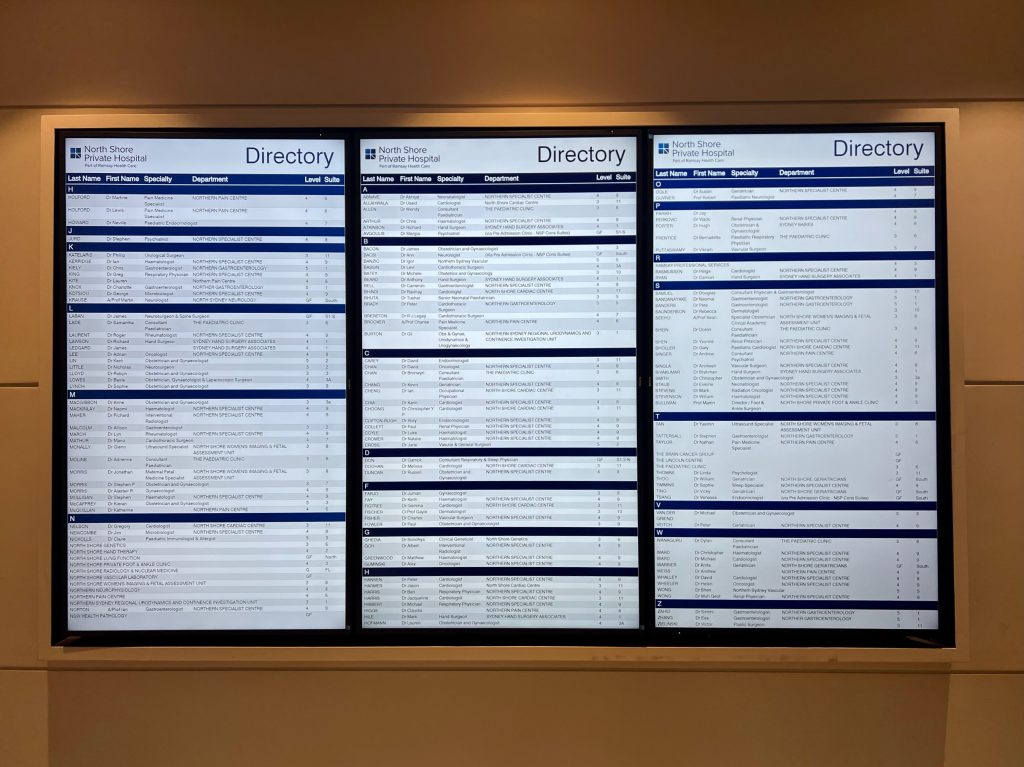 Three digital directory screens side by side in hospital reception area