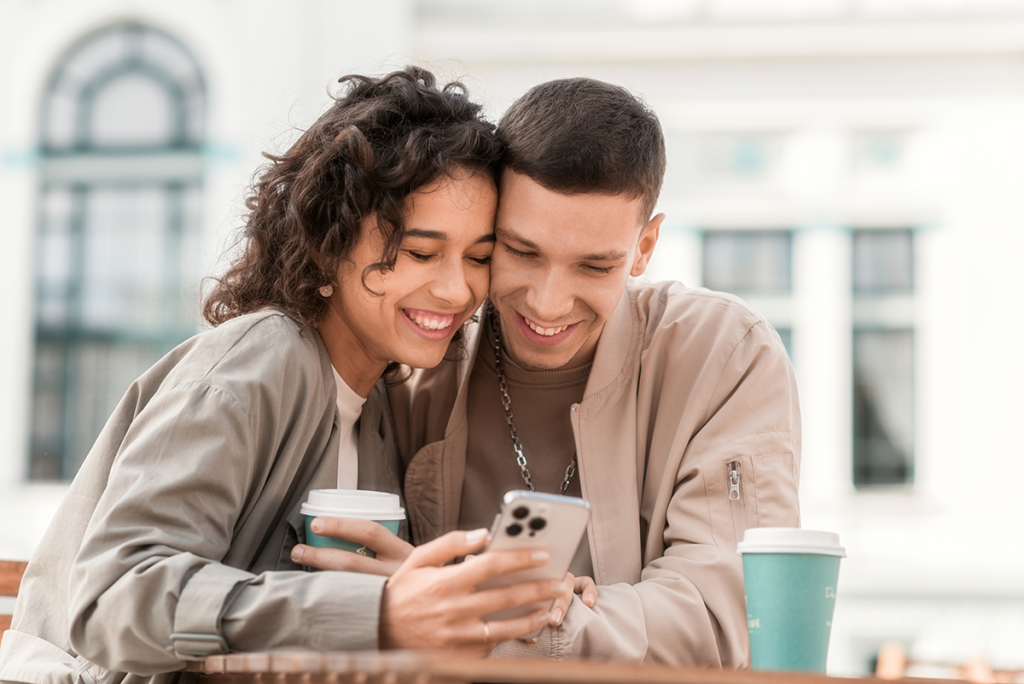 Happy couple outdoors near cafe smiling down at phone