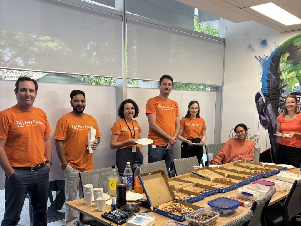 Five Faces team on Harmony day standing around meeting with room with pizza